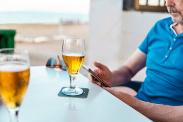 glass of cold beer on table and a man using his cell phone on the terrace bar
