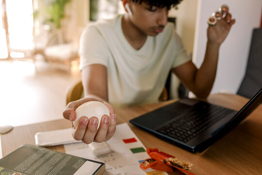 Autistic teenage boy holding ball while sitting by laptop in living room