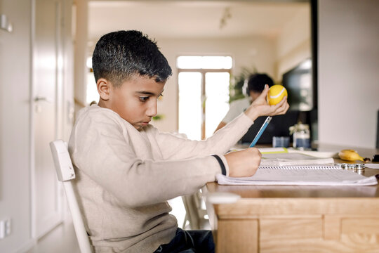 Boy learning while writing in book at home