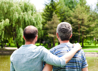 Adult father and son are hugging each other standing in the park. Back view.