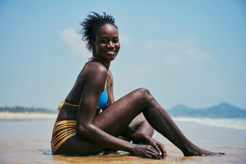 Sensual black model in swimsuit resting on sea shore
