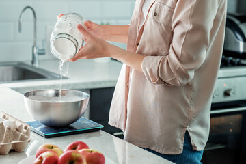 A woman in the kitchen adds rice flour to a bowl for making apple pie. Cooking