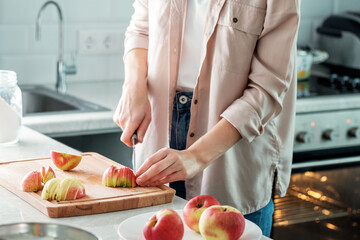 A woman in the kitchen slices fresh apples for making a pie.