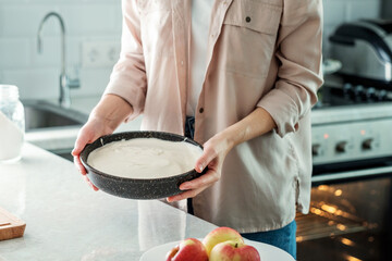 A woman in the kitchen holds a baking dish with a dough for making a pie with apples. Cooking food. Baking from rice flour