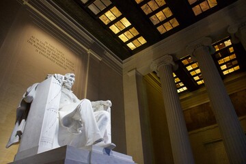 Statue of Abraham Lincoln inside the Lincoln Memorial, at dusk, with ceiling lighting.