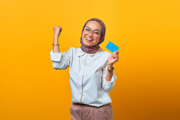 Portrait of cheerful Asian woman celebrating luck and holding blank card over yellow background