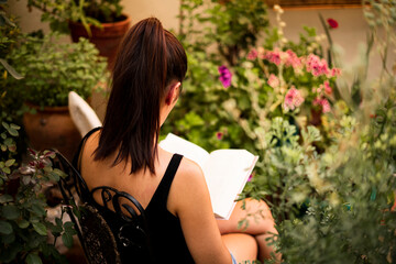 Relaxed woman reading a book in a nice patio surrounded by plants and flowers. 