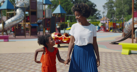 Afro mother and daughter holding hands walk at playground