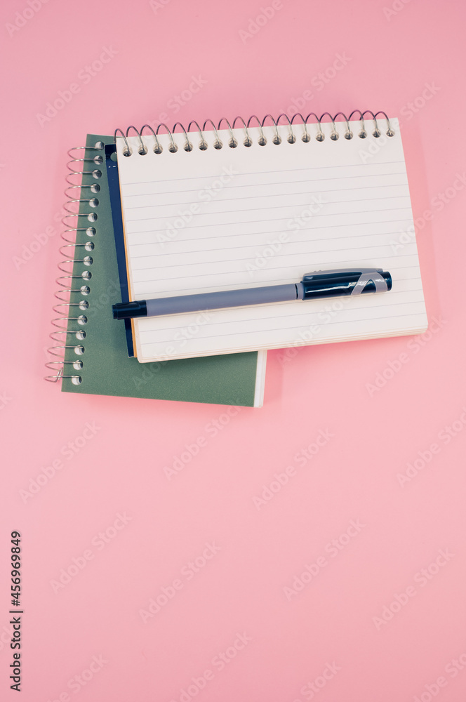 Poster vertical shot of an open notebook with a pen on a pink surface