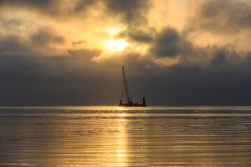 Fototapeta na wymiar Beautiful sunset in Arctic sea. Barge with crane. Golden hour. Construction Marine offshore works. Dam building, crane, barge, dredger.