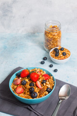 A bowl of mixed berries cereal and a small bowl of cereal with blueberries and a jar of cereal in the background