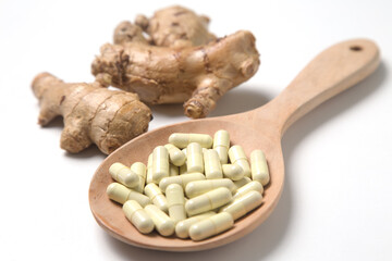 Capsule pills in wooden spoon with root ginger on white background.
