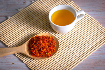 Safflower, False Saffron , Saffron Thistle in wooden spoon and a cup of tea.