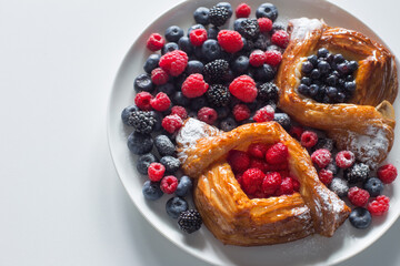 Danish with raspberries and blueberries on  round plate with berries on  white table
