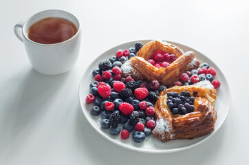 Danish with raspberries and blueberries with cup of tea on  white table