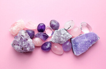 Obraz na płótnie Canvas Beautiful gemstones and druses of natural purple mineral amethyst on a pink background. Amethysts and rose quartz. Large crystals of semi-precious stones.