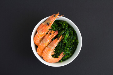 Top view of salad with seaweed and red shrimps in the white bowl on the black background.Close-up.