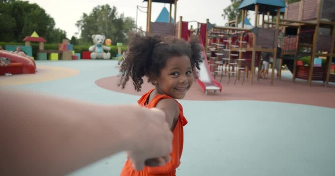 Pov shot of little afro girl holding mother hand walking on playground
