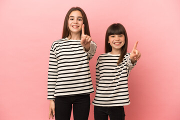 Little sisters girls isolated on pink background showing and lifting a finger
