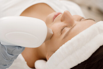 Young woman having laser hair removal procedure of face zone by specialist in cosmetic center....