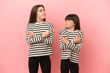 Little sisters girls isolated on pink background pointing to the laterals having doubts