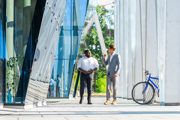 African-American businessman and his colleague in front of modern office building. Financial investors are talking outdoor. Banking and business concept.