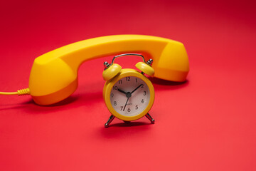Time to call. Yellow handset and alarm clock on a red background.