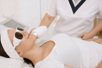 Young woman having laser hair removal procedure of face zone by specialist in cosmetic center....