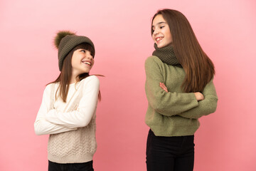 Little sisters wearing a winter clothes isolated on pink background looking over the shoulder with a smile