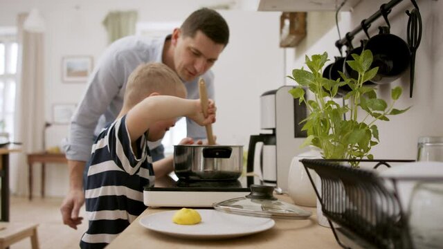 Father with happy down syndrome son indoors in kitchen, cooking.