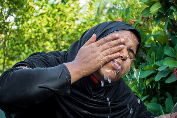 A woman splashes cold water on her face on a hot day. A Muslim woman dressed in black is performing...