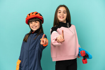 Little sisters practicing cycling and skater isolated on blue background showing and lifting a finger