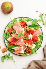 Sweet fig salad with jamon, blue cheese, walnuts, arugula on white background, top view, copy space