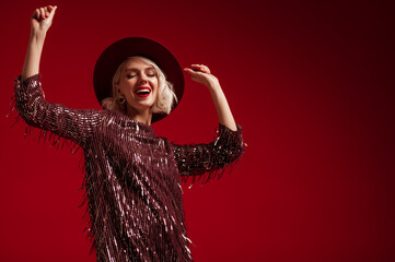Happy smiling fashionable blonde woman wearing trendy marsala color sequin mini dress, hat,...