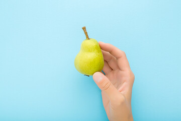 Young adult woman hand holding green pear on light blue table background. Pastel color. Closeup. Fresh fruit. Top down view.
