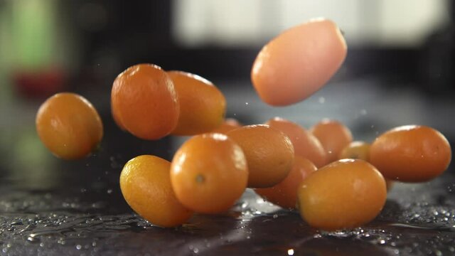 Freshly washed kumquats fall on a black slate. Water splashes..