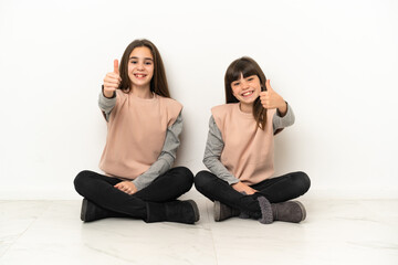 Little sisters sitting on the floor isolated on white background giving a thumbs up gesture because something good has happened