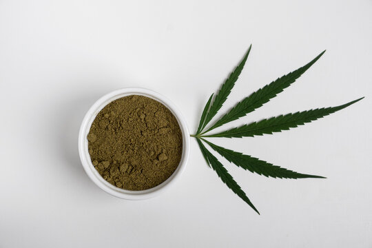 Hemp flour in a cup and leaves on a white background top view. Copy space, no people, horizontal orientation, top view, flatlay