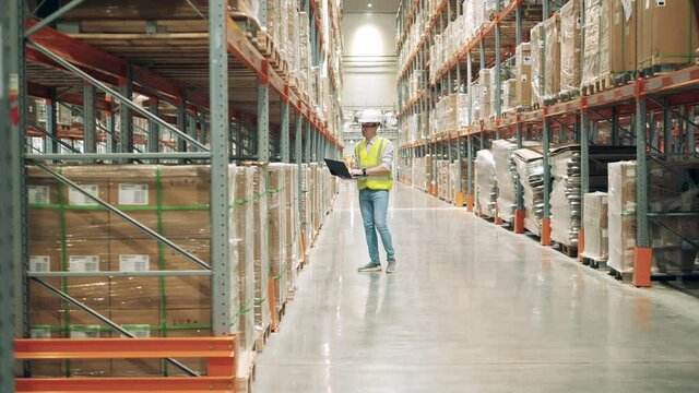 Storage worker with a laptop is observing shelves with parcels