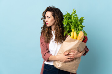 Young woman holding a grocery shopping bag isolated on blue background looking to the side