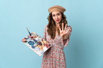 Young artist girl holding a palette isolated on blue background happy and counting four with fingers