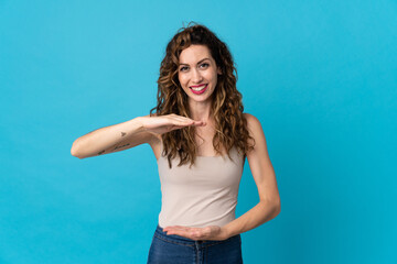 Young caucasian woman isolated on blue background holding copyspace imaginary on the palm to insert an ad