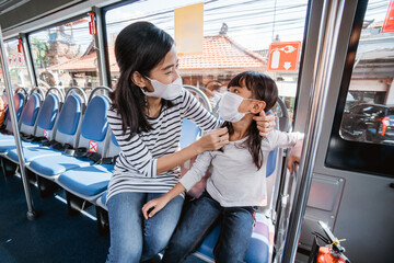 asian mother taking her daughter to school by riding bus public transport wearing a face mask