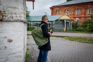 A man businessman in a blue coat with green backpack on his back stands outside and looks into the...