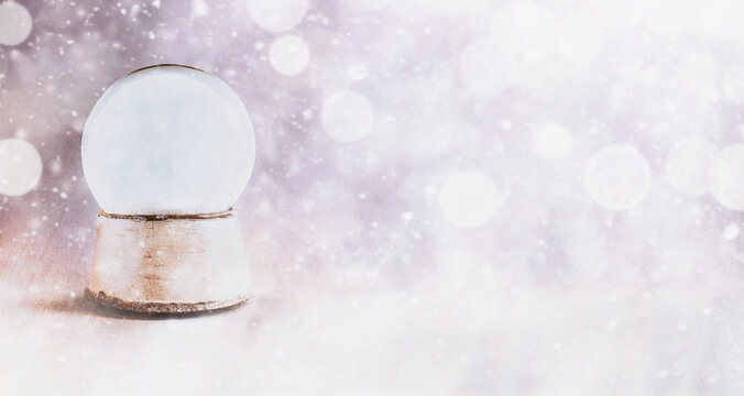 Magical empty snow globe over a textured background banner with falling snow and streams of light and glitter. Copy space available.