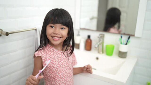 asian little girl brushes her teeth alone in the bathroom