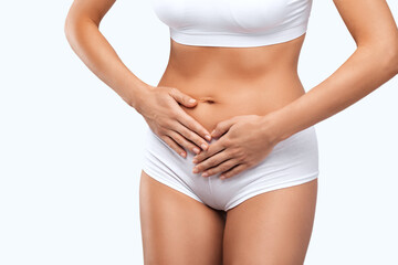 A slender beautiful woman in white underwear is holding her stomach, she has a stomach ache.