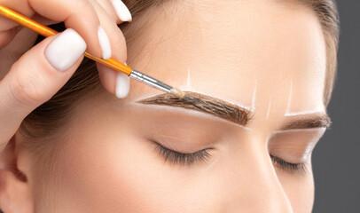 Make-up artist makes markings with white pencil for eyebrow and paints eyebrows. Professional...