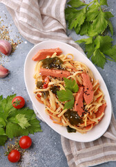 Healthy food. Wok noodles with vegetables, red fish, seaweed, sesame seeds on a white plate on a light gray background. Fresh herbs, garlic, tomato, curly kale cabbage, celery. Background image
