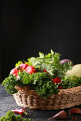 Fototapeta na wymiar Harvest. Fresh herbs and vegetables. Curly kale cabbage, parsley, celery, red pepper, cucumbers, zucchini, garlic in a basket on a black table. Background image, copy space